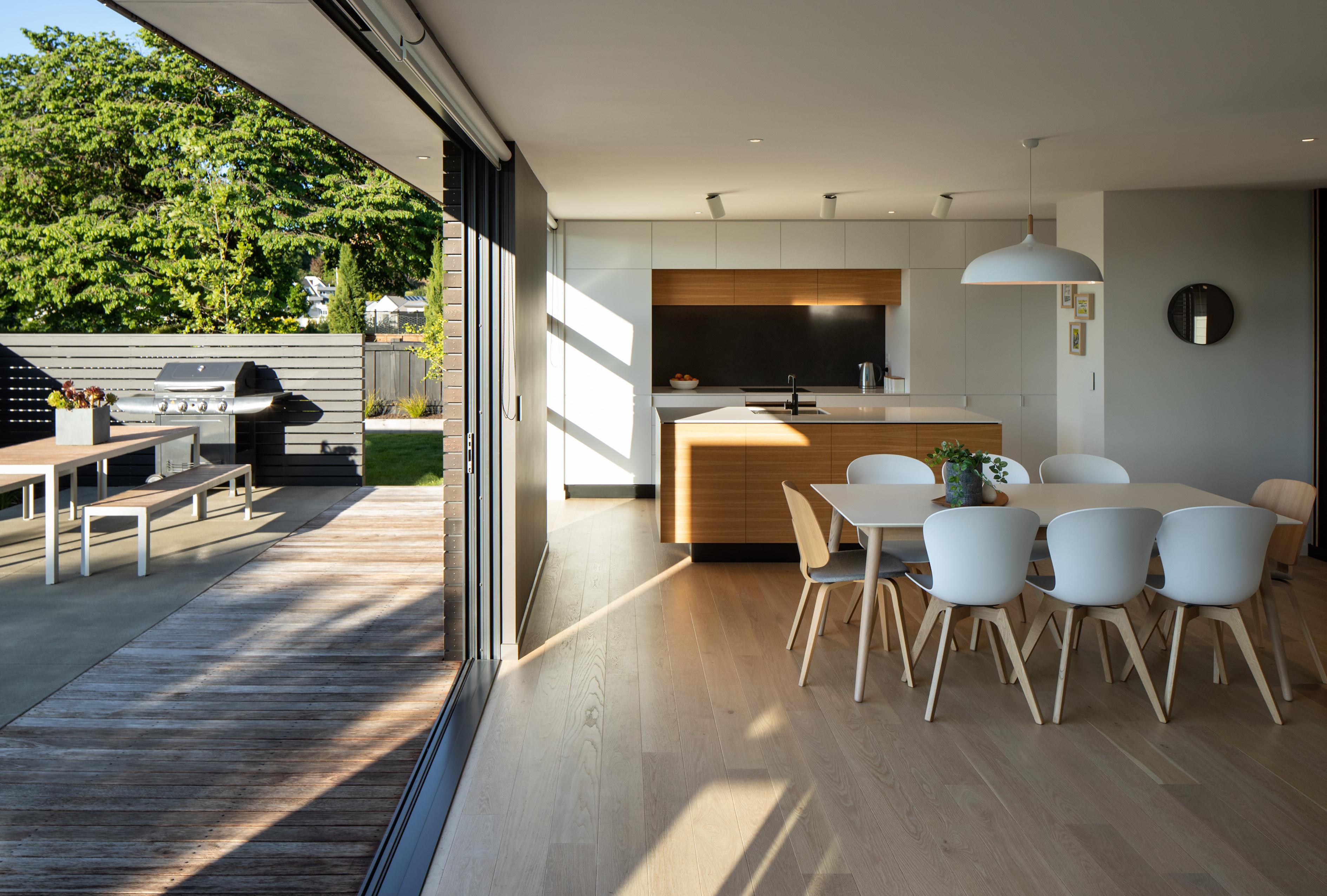 Interior of the kitchen and dining area, with sliding door opened to an outdoor living area with seating and barbecue