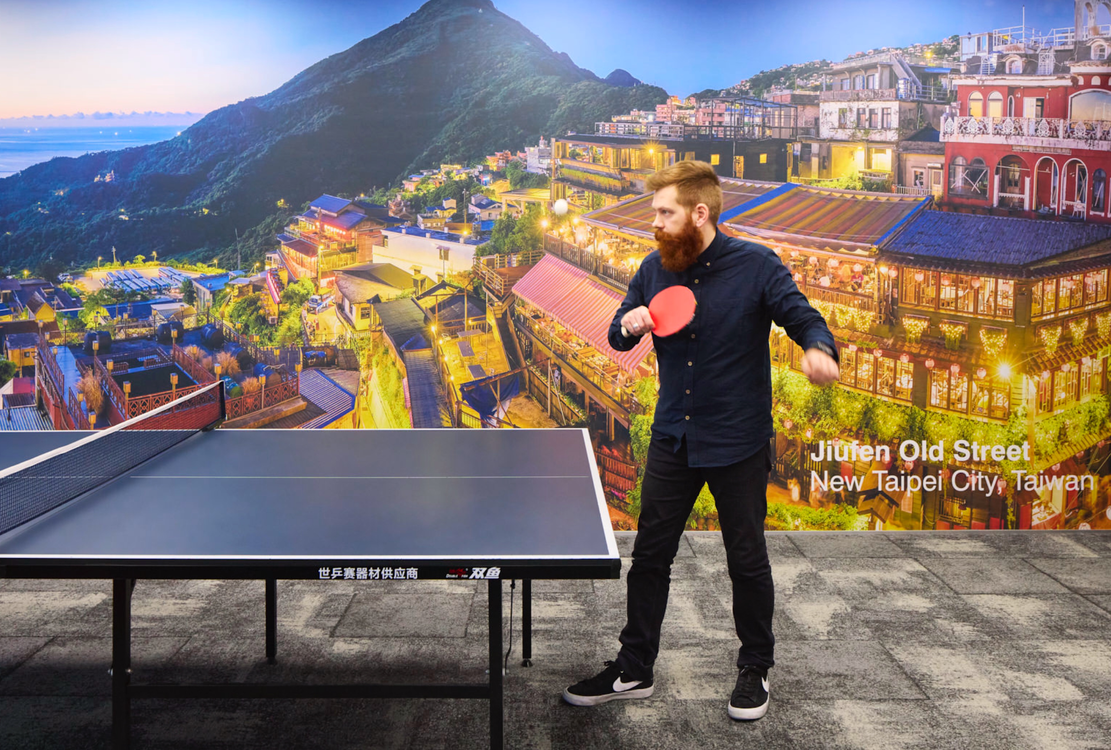 Man playing table tennis with supergraphic of Jiufen Old Street in background