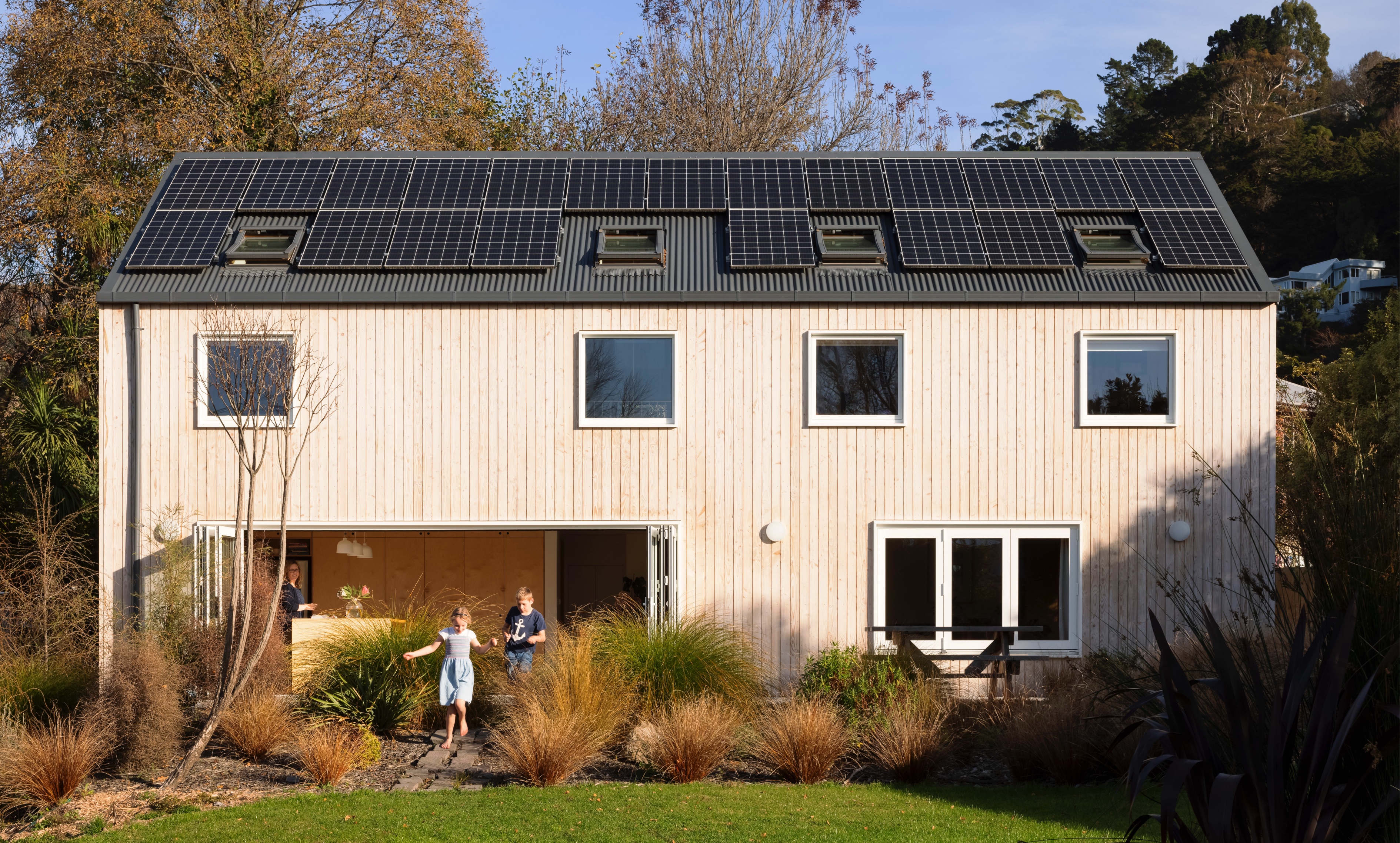 Exterior of house with photovoltaic panels, and children skipping out of open sliding door